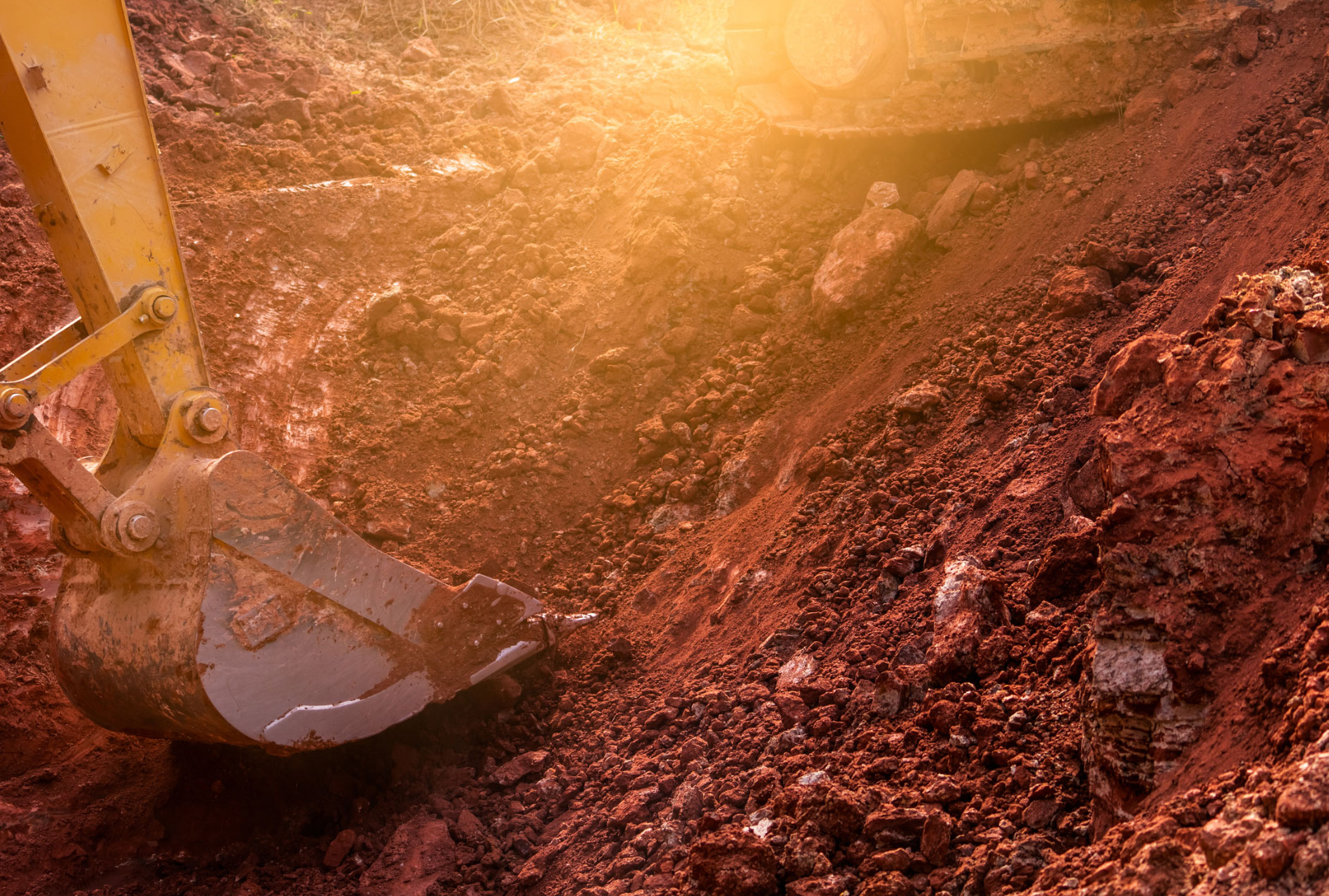 An M Lato Excavating & Tree Care Service excavator is digging soil at a construction site, with sunlight beautifully illuminating the scene.