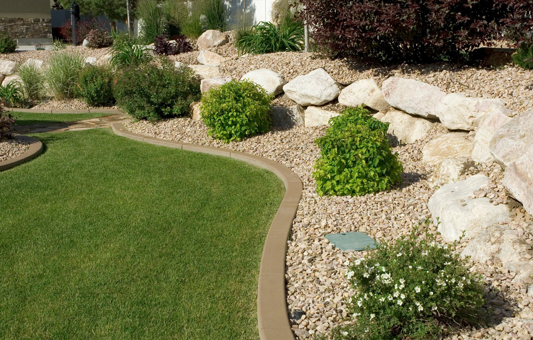 A neatly landscaped yard with a curved grass path, bushes, rocks, and gravel showcases expert Tree Care by M Lato Excavating & Tree Care Service.
